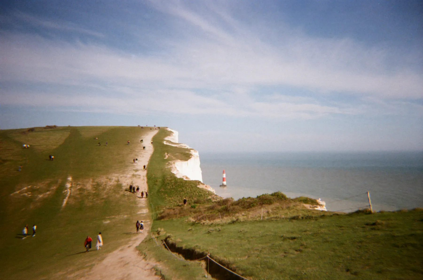Walkers along a grassy cliff with a lighthouse offshore